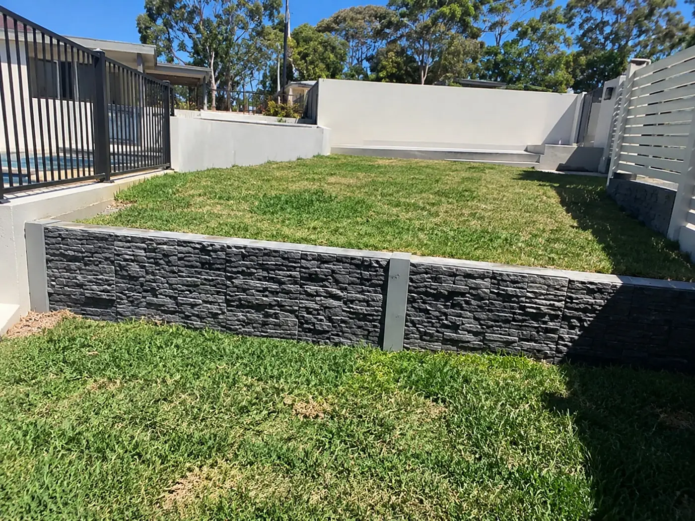 Low concrete retaining wall holding a level lawn beside a pool fence