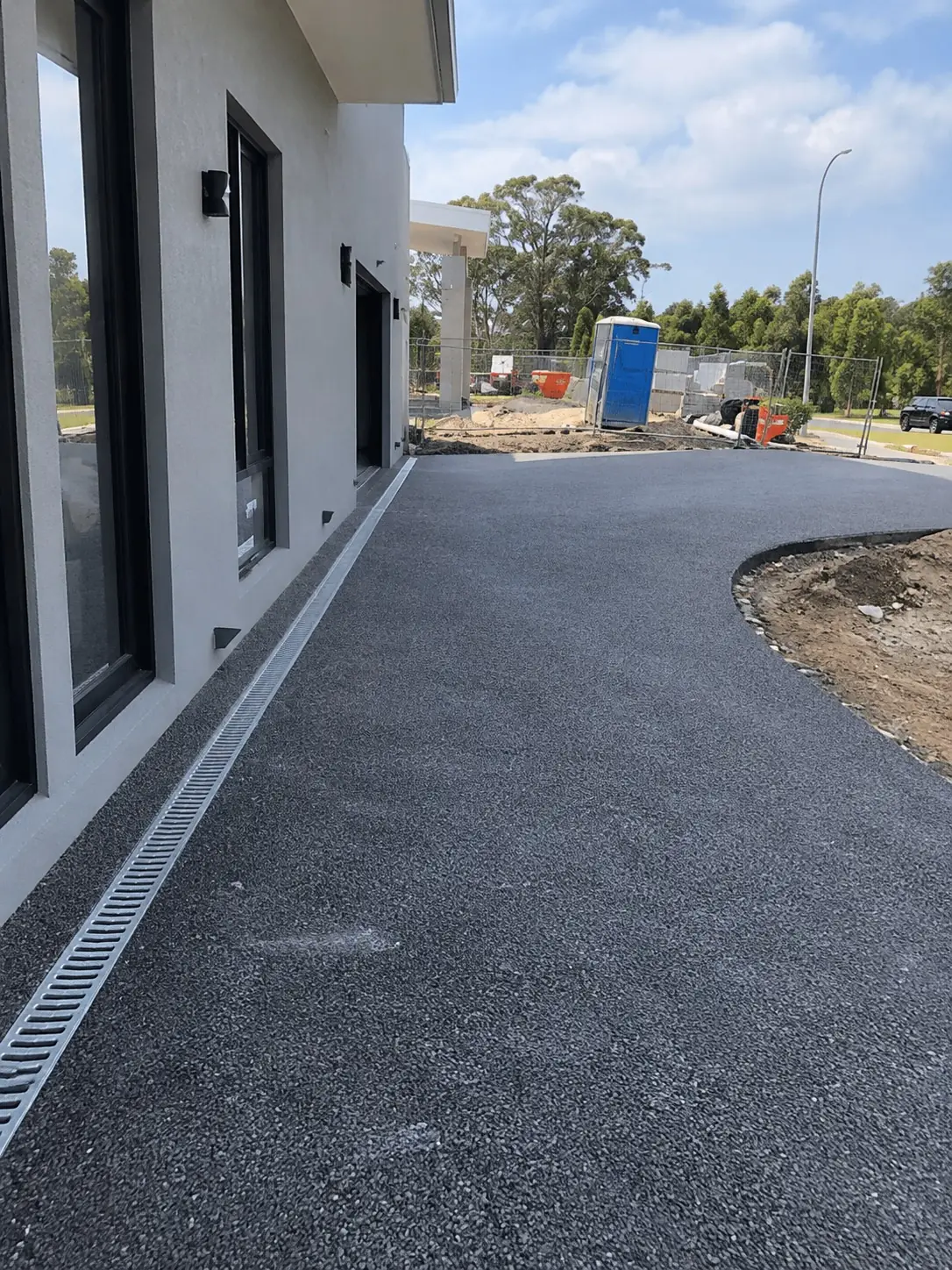 New asphalt driveway and strip drain beside a modern home